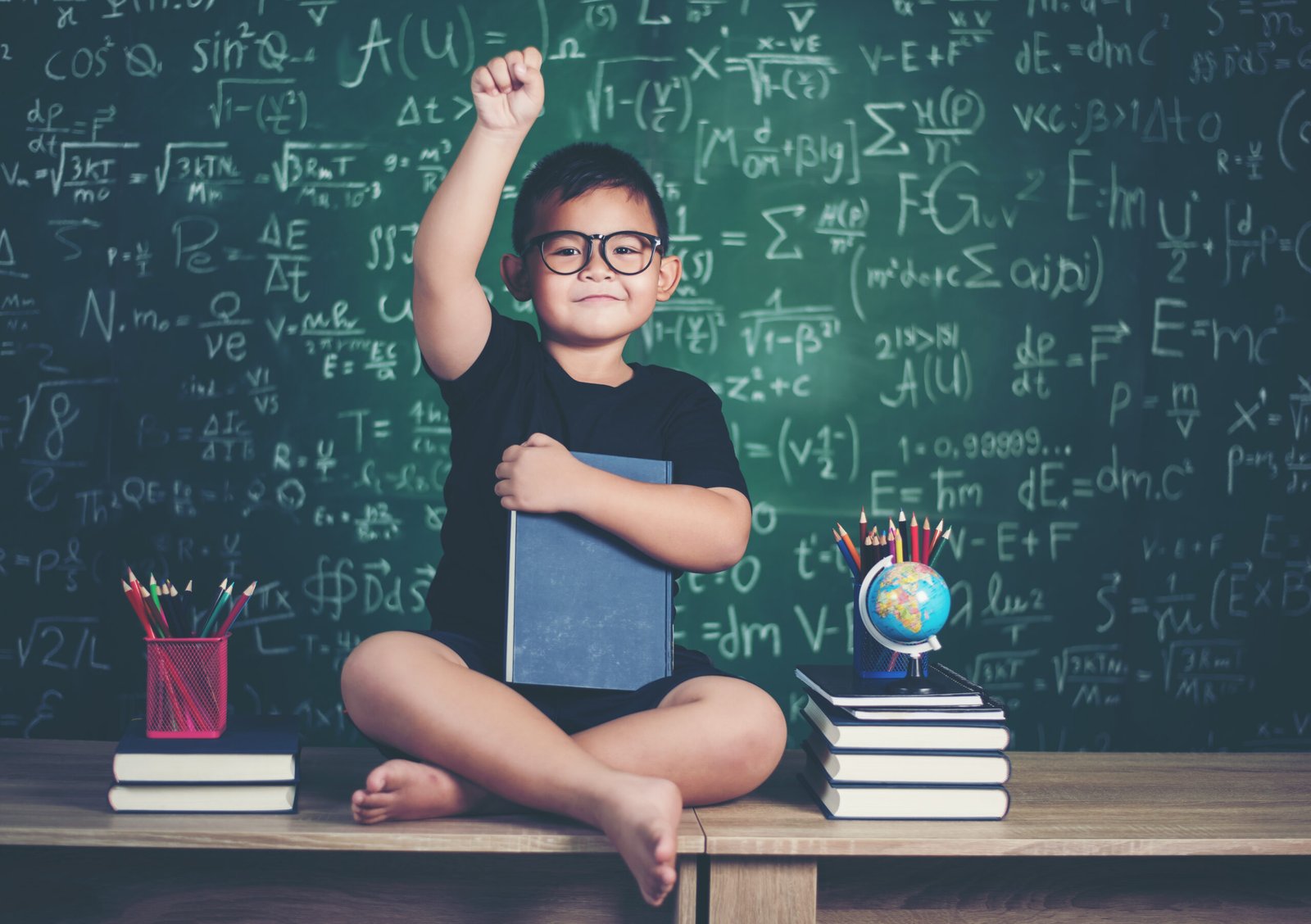 boy with books sitting near green chalkboard